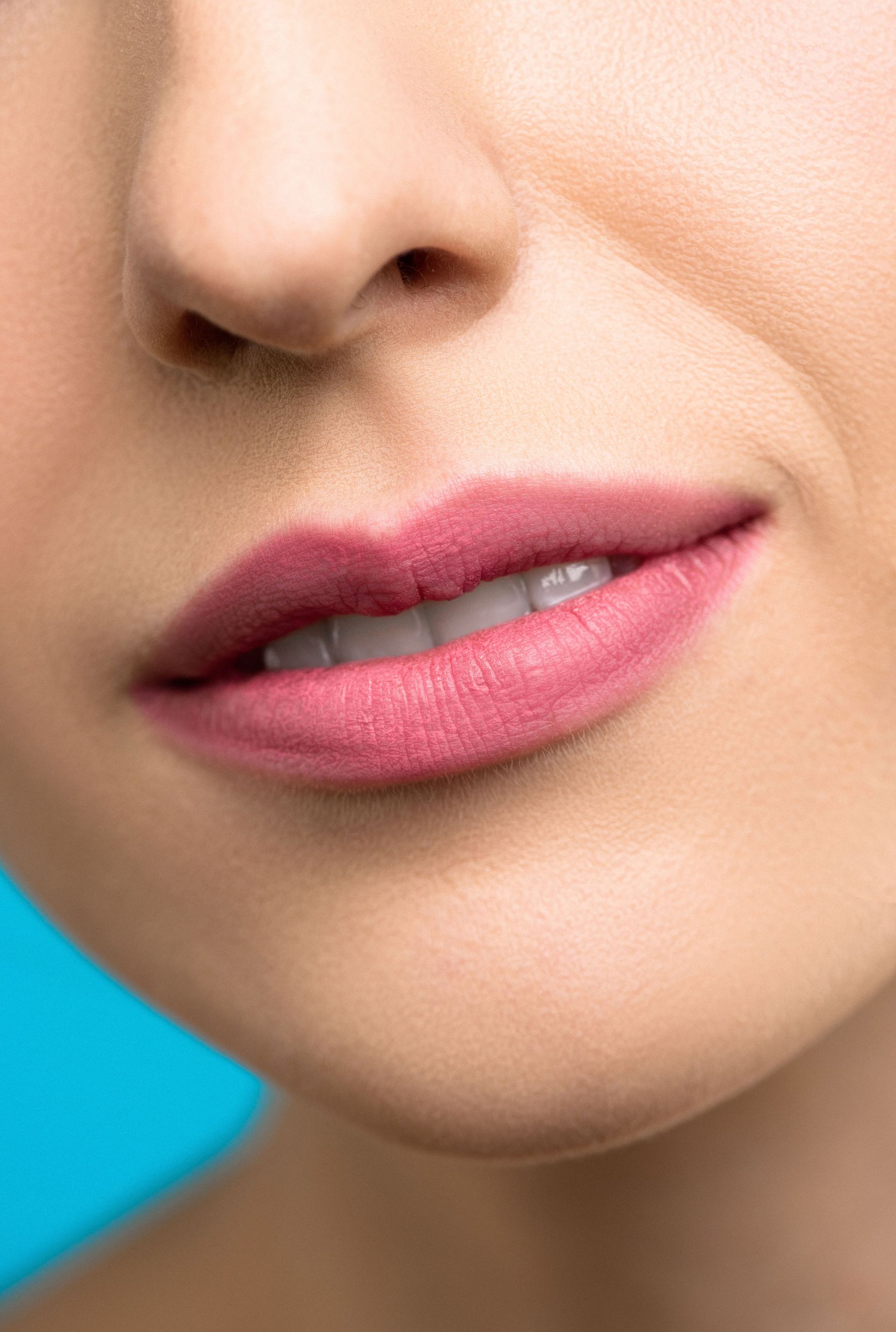 A detailed close-up of a woman's smile with pink lipstick against a blue background.