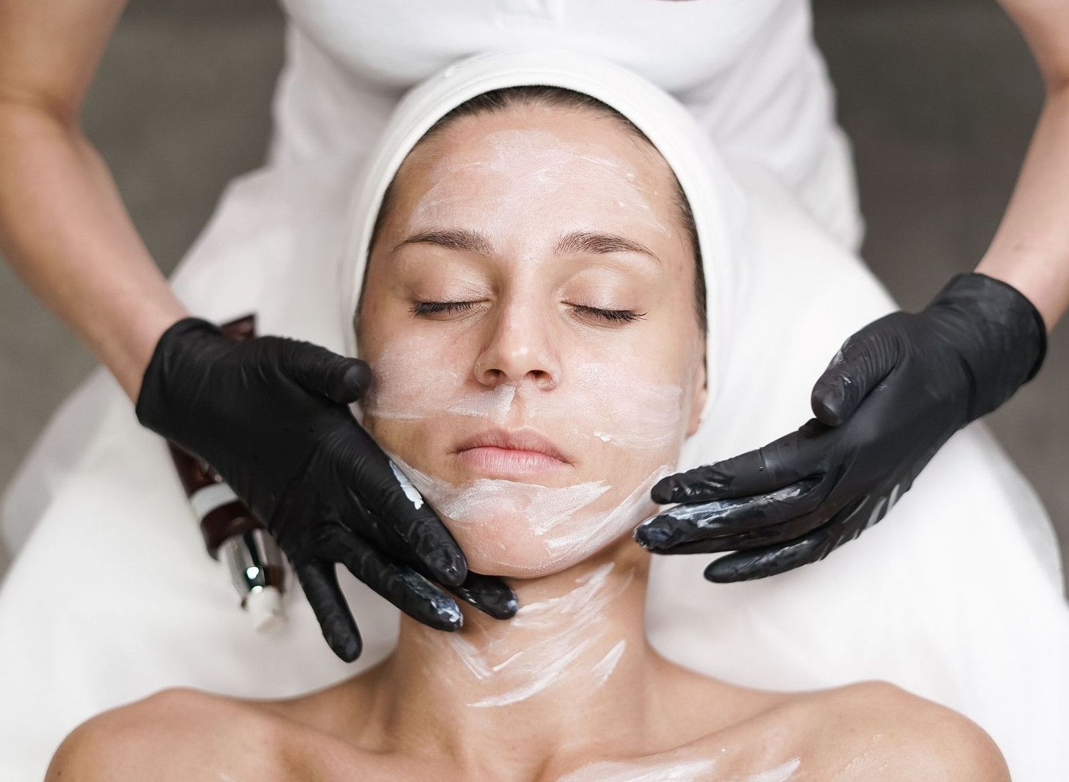 Woman receiving a facial treatment at spa, with beautician applying mask in a relaxing setting.